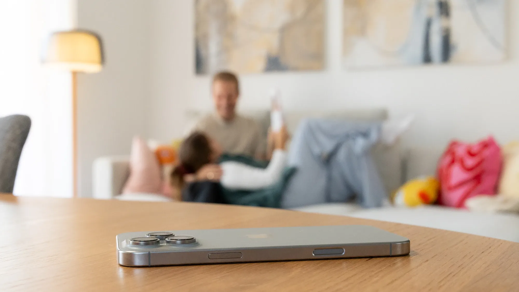 Das Handy liegt auf dem Tisch, im Hintergrund entspannt die Familie auf dem Sofa